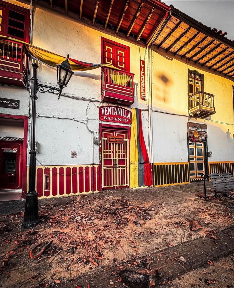 Esquina de fachada amarilla y roja en Salento con escombros acumulados en el andén